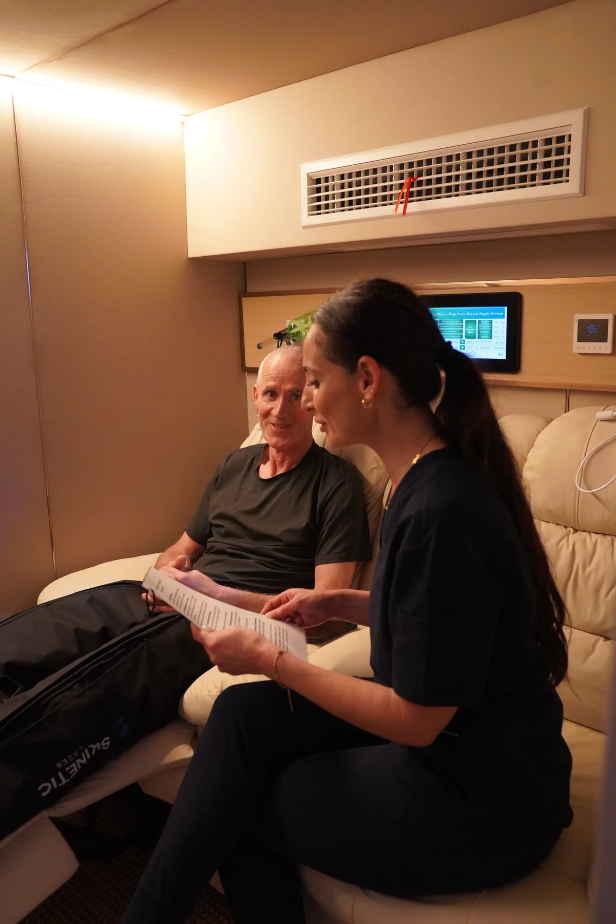 Nurse speaking with a seated client inside My BioHealth’s chamber, with recovery boots visible.