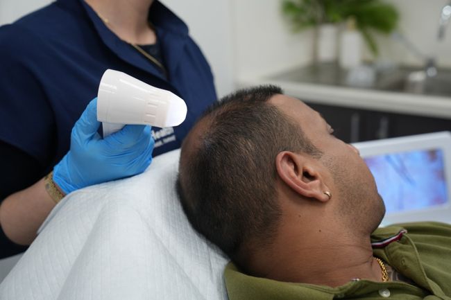 A practitioner examining a client’s scalp with a handheld assessment device at My BioHealth