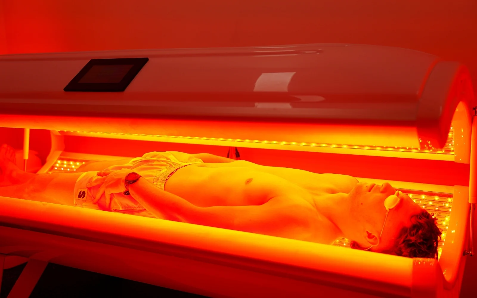 Client lying in the full-body red light bed with eye protection